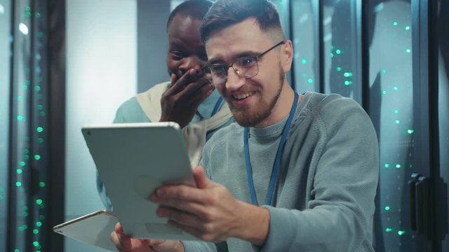 Crazy positive server technicians laughing hard browsing fun content on digital tablet in data center. Friendly team of database specialists.