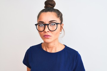 Beautiful woman with bun wearing blue t-shirt and glasses over isolated white background with a confident expression on smart face thinking serious