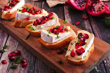 Holiday crostini appetizers with brie cheese, pomegranates and parsley. Close up on a serving board against a rustic wood background. Party food concept. - obrazy, fototapety, plakaty