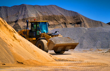 Sand quarry, excavating equipment, bulldozer with heap of sand in background. Selective focus. - obrazy, fototapety, plakaty