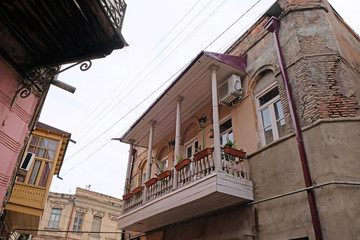 Fototapeta na wymiar An old building with a small balcony with wooden pillars. Small flowerpots on an old painted balcony. Ancient architecture in the center of Tbilisi.