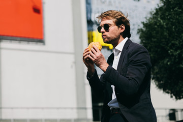 A Guy In A Suit Eats A Hamburger Outside On A Sunny Day