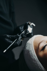 The black-gloved microblading master holds a manipulator for further drawing eyebrows along the finished contour, previously drawn on the front surface of the model.