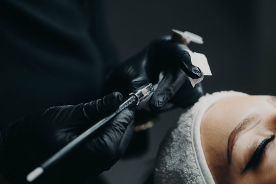 The black-gloved microblading master holds a manipulator for further drawing eyebrows along the finished contour, previously drawn on the front surface of the model.