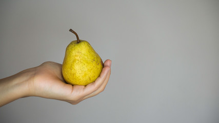 Hand of a white woman holding yellow pear on a grey background.