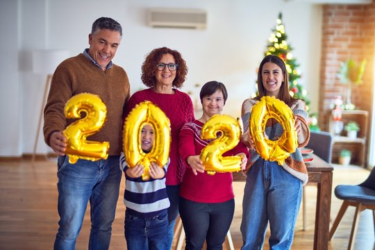 Beautiful family smiling happy and confident. Standing and posing holding 2020 balloons celebrating new year around christmas tree at home
