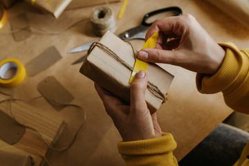 Woman packaging box. Kraft wrapping paper and natural twine. Recycling material. Happy holiday...