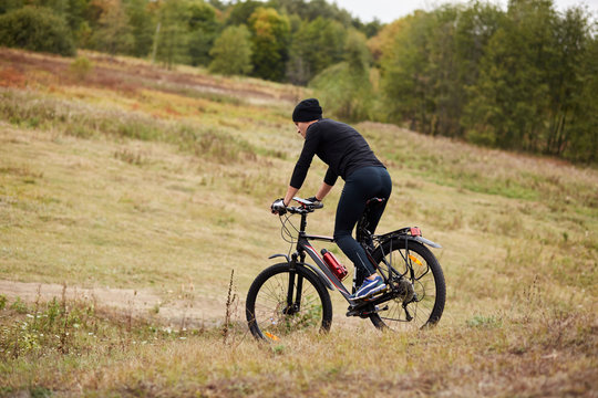 Image of mauntain bike cyclist in meadow near forest, side view of sporty male riding bike during his vacation, enjoying his hobby, rides downhill, covering assigned distance. Lifestyle concept.