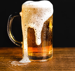 Cold beer with foam in a mug, on a wooden table and a dark background with blank space for a logo...