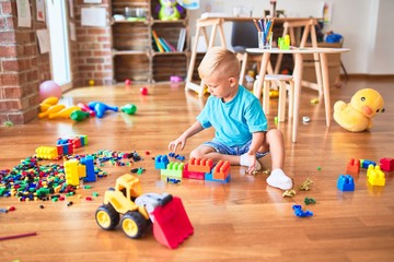 Young caucasian kid playing at kindergarten with toys. Preschooler boy happy at playroom.