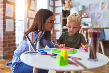 Young caucasian child playing at playschool with teacher. Mother and son at playroom drawing a draw...