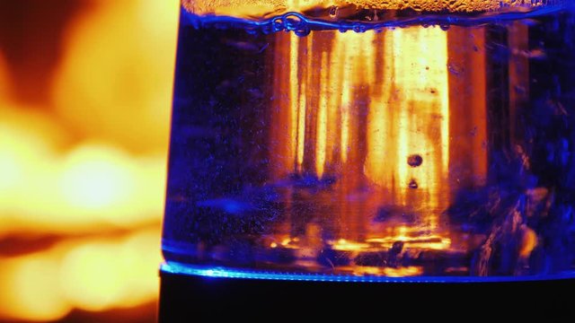 Boiling water in a glass teapot on a background of fire in a fireplace insert