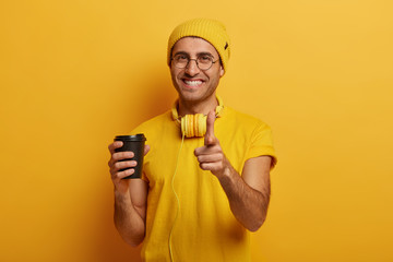 Positive handsome hipster guy points fore finger at you, makes choice, wears yellow hat, t shirt...