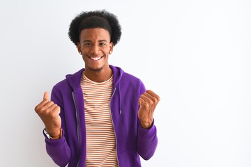 African american man wearing purple sweatshirt standing over isolated white background celebrating surprised and amazed for success with arms raised and open eyes. Winner concept.
