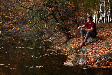 A man sits on the bank of the river in the autumn and looks into the distance, a photo in warm colors