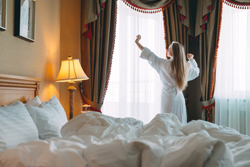 Woman in bathrobe stay near the window in hotel room.