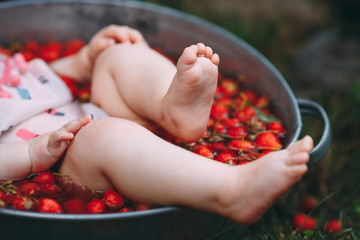 A little girl bathes in a basin with strawberries in the garden.