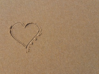 Top view photo of a heart symbol hand-drawn on the sand. Romantic photo background with space for adding text. Beach sand texture / background.