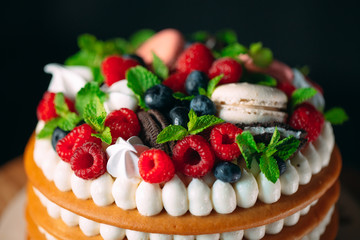 Fruit cake. Cake decorated with berries on a wooden stand on a black background.