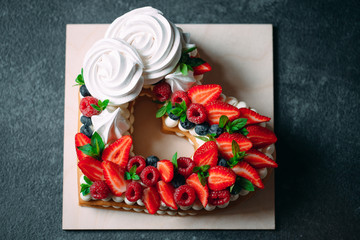 Fruit cake. Cake decorated with berries on a wooden stand on a black background.