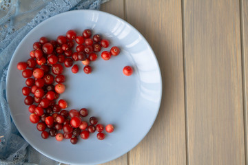 Red cranberries on blue plate top view on wooden background.