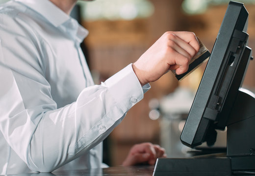 small business, people and service concept - happy man or waiter in apron at counter with cashbox working at bar or coffee shop.