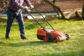 mowing trimmer - worker cutting grass in green yard at sunset. Man with electric lawnmower, lawn mowing. Gardener trimming a garden.