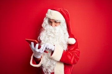 Middle age man wearing Santa Claus costume using tablet over isolated red background with a happy face standing and smiling with a confident smile showing teeth