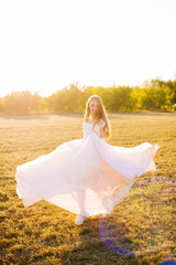 Fototapeta na wymiar Beautiful blonde bride, feelling cheerful and dancing in field on sunlights