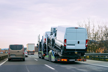 Minivan carrier transporter truck in road. Auto vehicles hauler on driveway. European van transport...