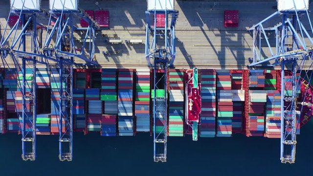 Aerial top down pan video of industrial container loading and unloading to tanker ships logistics terminal