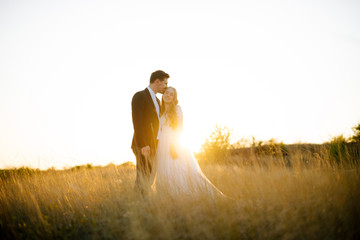 Beautiful photo of bride and groom, standing in  field and hugging, with sunset lights on background