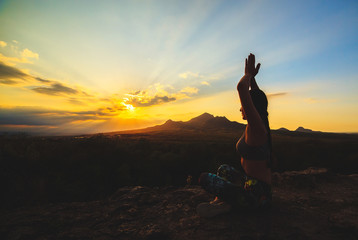 Young woman practicing yoga or pilates at sunset or sunrise in beautiful mountain location.