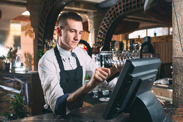 small business, people and service concept - happy man or waiter in apron at counter with cashbox...
