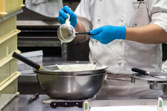 A male pastry chef using a spatula and ladle while making whipped cream.