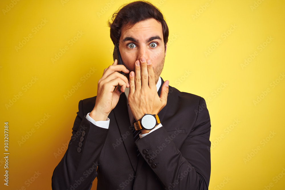 Poster Young handsome businessman talking on the smartphone over isolated yellow background cover mouth with hand shocked with shame for mistake, expression of fear, scared in silence, secret concept