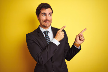 Young handsome businessman wearing suit and tie standing over isolated yellow background Pointing aside worried and nervous with both hands, concerned and surprised expression