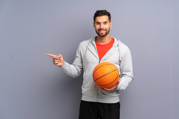 Handsome young basketball player man surprised and pointing finger to the side