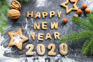 The concept 2020. Baked letters Happy New year and numbers 2020.Greeting card with gingerbread.Christmas card made of gingerbread on a wooden table surrounded by fir branches, nuts, spices and orange.