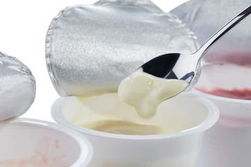 Creamy yogurt with banana flavor in a spoon on the background of open plastic cups with yogurts of different flavors.