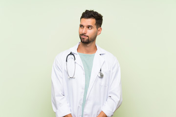 Fototapeta premium Young doctor man over isolated green wall standing and looking to the side
