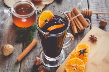 Hot mulled wine with orange, cinnamon, honey and anise on wooden background.