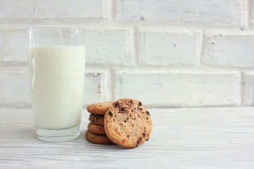 Glass of milk and chocolate chip cookies on wooden table against white brick wall background