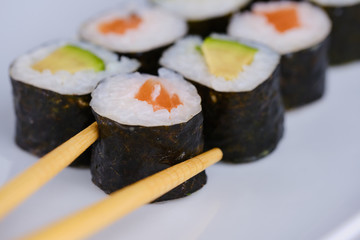 Sake maki Japanese roll with salmon and avocado, wooden chopsticks taking one roll