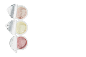 Obraz na płótnie Canvas Yogurts of three different flavors in open plastic cups isolated on a white background. Top view. Copy space.