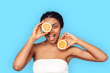 Beauty Concept. Young african woman isolated on blue covering eye with lemon smiling playful