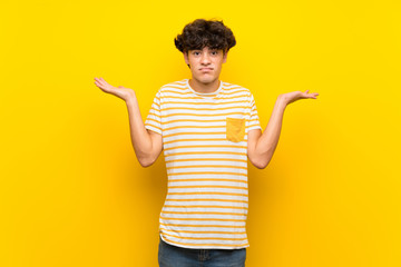 Young man over isolated yellow wall having doubts while raising hands