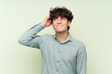 Young man over isolated green wall having doubts and with confuse face expression