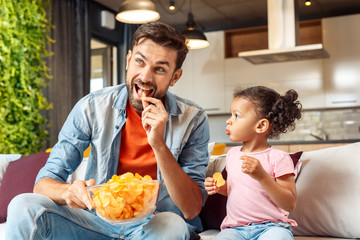 Father and little daughter eating chips at home