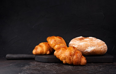 Fresh round bread and croissants on dark table. Copy space.